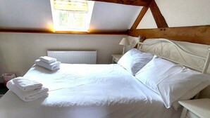 A neatly made bed with white linens and pillows, a bedside lamp, and a radiator in a room with wooden beams on the ceiling. - 1 Bed in Cradley (oc-s45723) (Cradley and Storridge)