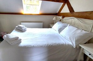 A neatly made bed with white linens and pillows, a bedside lamp, and a radiator in a room with wooden beams on the ceiling. - 1 Bed in Cradley (oc-s45723) (Cradley and Storridge)