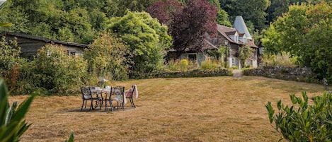 A grassy backyard with a dining table and chairs, surrounded by trees and a house.