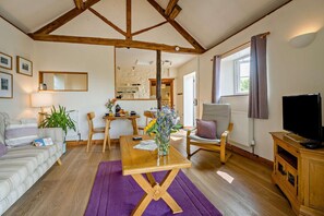 A cozy living room with a wooden dining table, a sofa, a TV, and a kitchen in the background. - 1 Bed in Cradley (oc-c45724) (Cradley and Storridge)