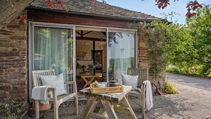 A stone building with a wooden deck, two chairs, a table, and a window. - 1 Bed in Cradley (oc-c45724) (Cradley and Storridge)