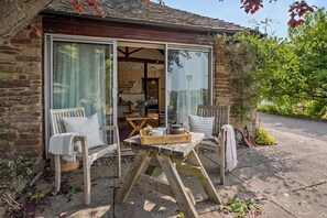 Ein Gebäude aus Stein mit einer Holzterrasse, zwei Stühlen, einem Tisch und einem Fenster.