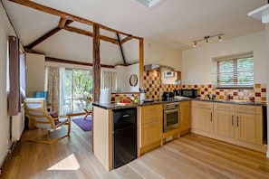 A kitchen with wooden cabinets, a built-in oven, a microwave, and a dining area with a chair and table. - 1 Bed in Cradley (oc-c45724) (Cradley and Storridge)