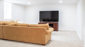 Una sala de estar con un sofá modular, un televisor de pantalla plana sobre un mueble de madera y un ventanal grande.
