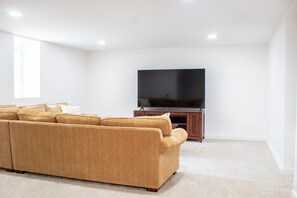 A living room with a sectional sofa, a flat-screen TV on a wooden stand, and a large window.