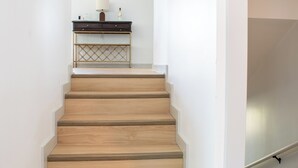 Una escalera con escalones de madera que conduce a una consola oscura con una lámpara y una botella encima.