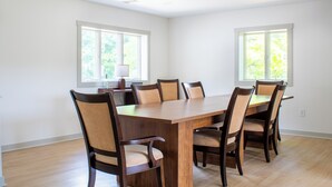 Un comedor amplio con una gran mesa de madera y seis sillas, ventanas amplias con persianas, y una lámpara en el techo.