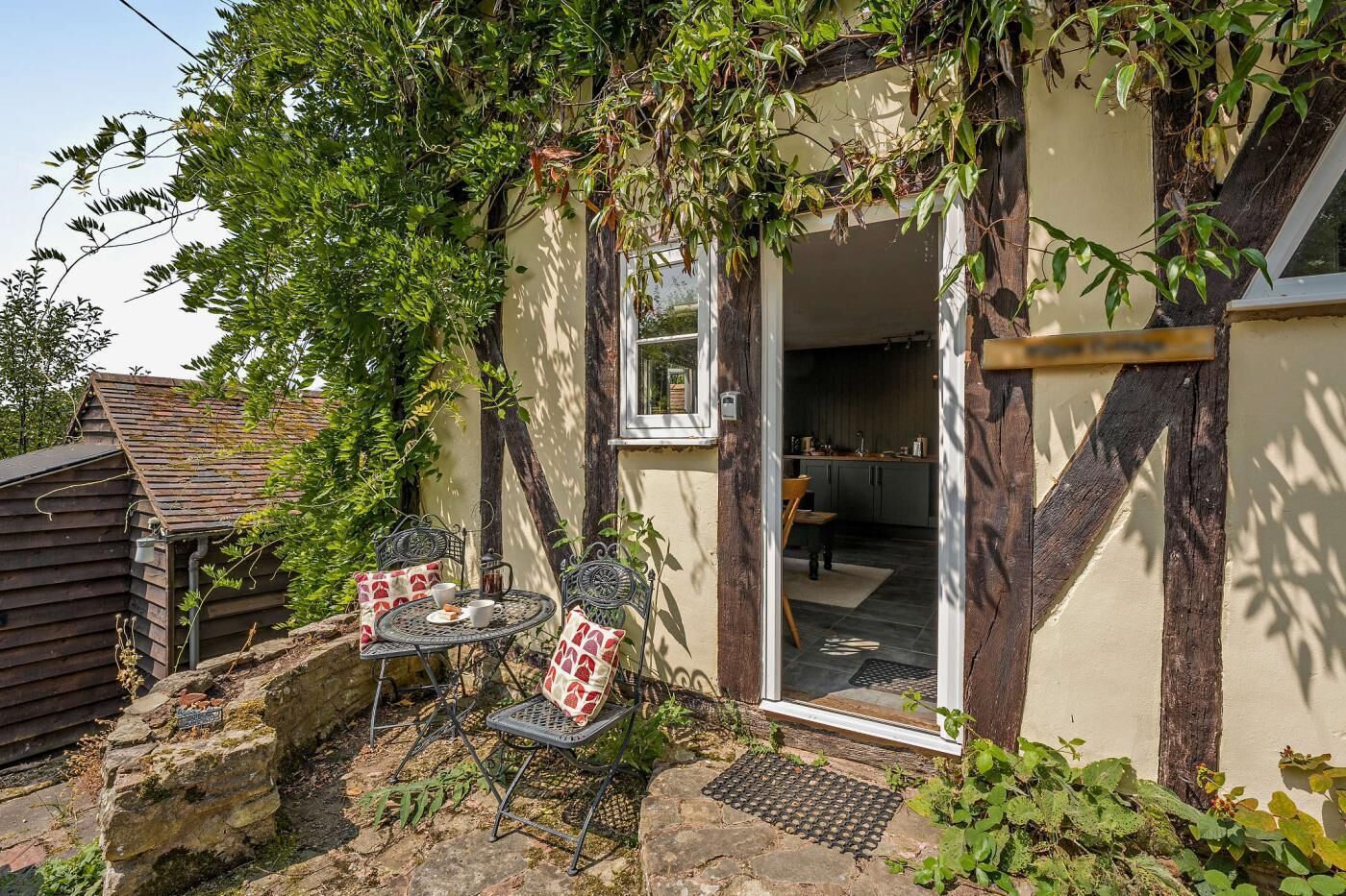 Ein rustikales Cottage mit einer Steinterrasse, einem Esstisch mit Stühlen und einer durchgehenden Tür erkennbaren Küche.