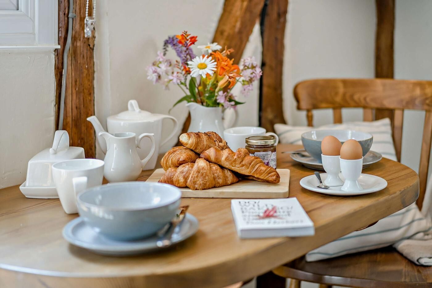 A breakfast setup with croissants, eggs, and a vase of flowers on a wooden table.