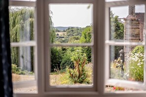 Une vue à travers une fenêtre donnant sur un mur de pierre et de la verdure à l’extérieur.