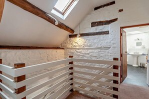 Eine Treppe mit weißen Geländern und Holzbalken, die zu einem Raum mit weißer Ziegelwand und einem Oberlicht führt.