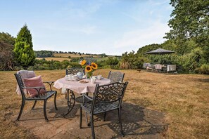 Eine Außenpatio mit einem runden Tisch für zwei Personen, umgeben von Stühlen, und ein kleiner Tisch mit einem Stuhl im Hintergrund.