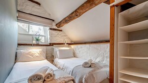 Een slaapkamer met twee bedden, een raam met een plant en een plafond met houten balken.