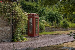Une cabine téléphonique rouge, située dans un jardin, avec un mur de pierres et de la verdure.