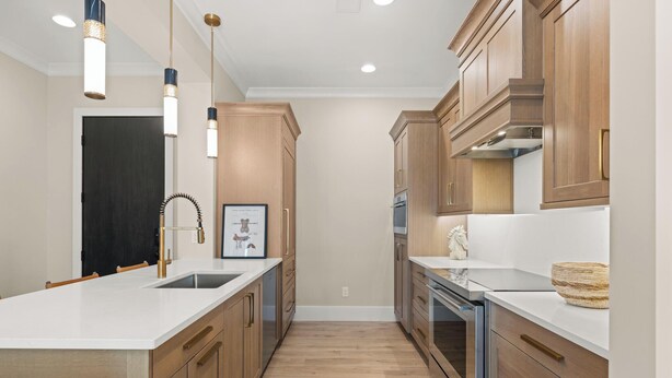 A narrow kitchen with wooden cabinets, a stainless steel sink, and pendant lighting.