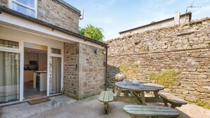 Ein Steinhaus mit einer Terrassenfläche, ausgestattet mit einem Holztisch und Bänken.