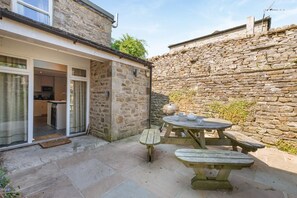 Ein Steinhaus mit einer Terrassenfläche, ausgestattet mit einem Holztisch und Bänken.
