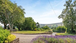 A rural landscape with a stone pathway, lavender bushes, and a grassy area with trees.