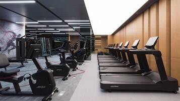 Academia com várias esteiras alinhadas a uma parede de madeira, bicicletas ergométricas e máquinas de musculação.