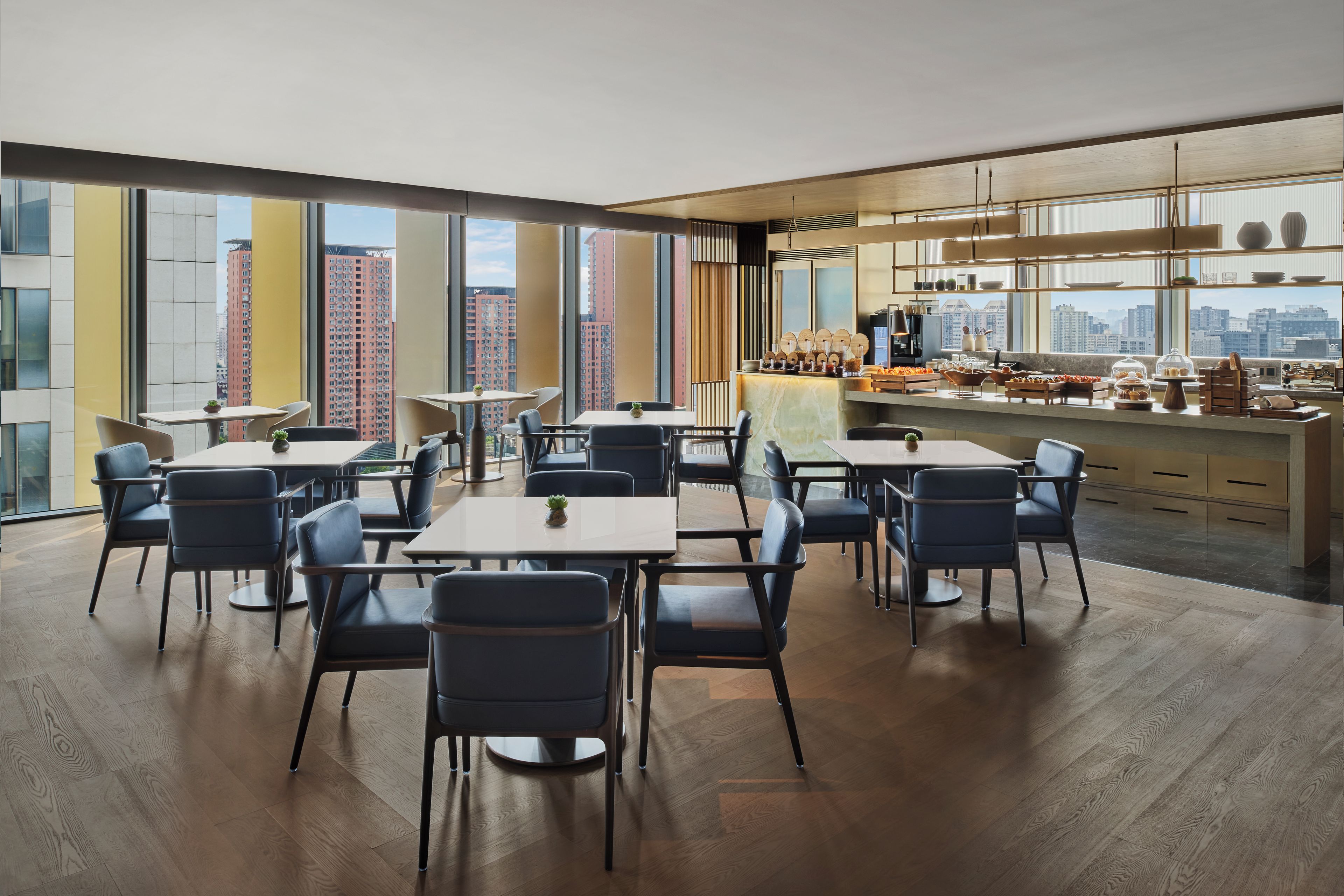 A modern dining area with high ceilings, large windows, and a city view.
