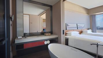 Quarto de hotel moderno com uma banheira grande, cama com lençóis brancos e um espelho amplo que reflete o ambiente.