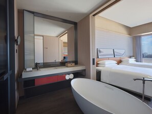 A modern hotel room with a large bathtub, a bed with white linens, and a large mirror reflecting the room.