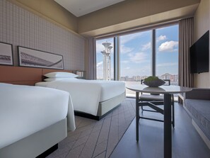 Habitación de hotel con dos camas, una mesa de comedor y un ventanal con vistas a la ciudad.