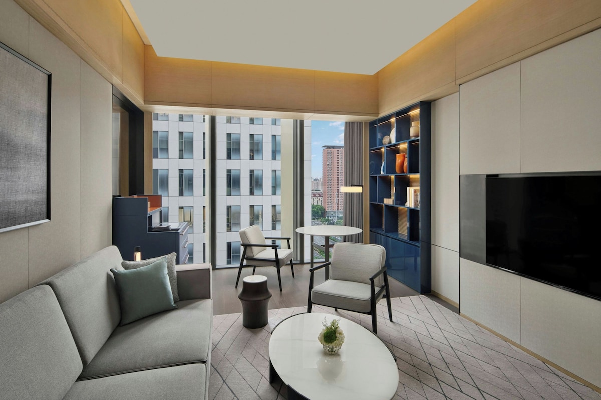 A modern living room with a sofa, chairs, a coffee table, a bookshelf, and a TV.