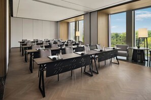 Un salón de conferencias con varias mesas y sillas, ventanas amplias y vistas al exterior con vegetación.