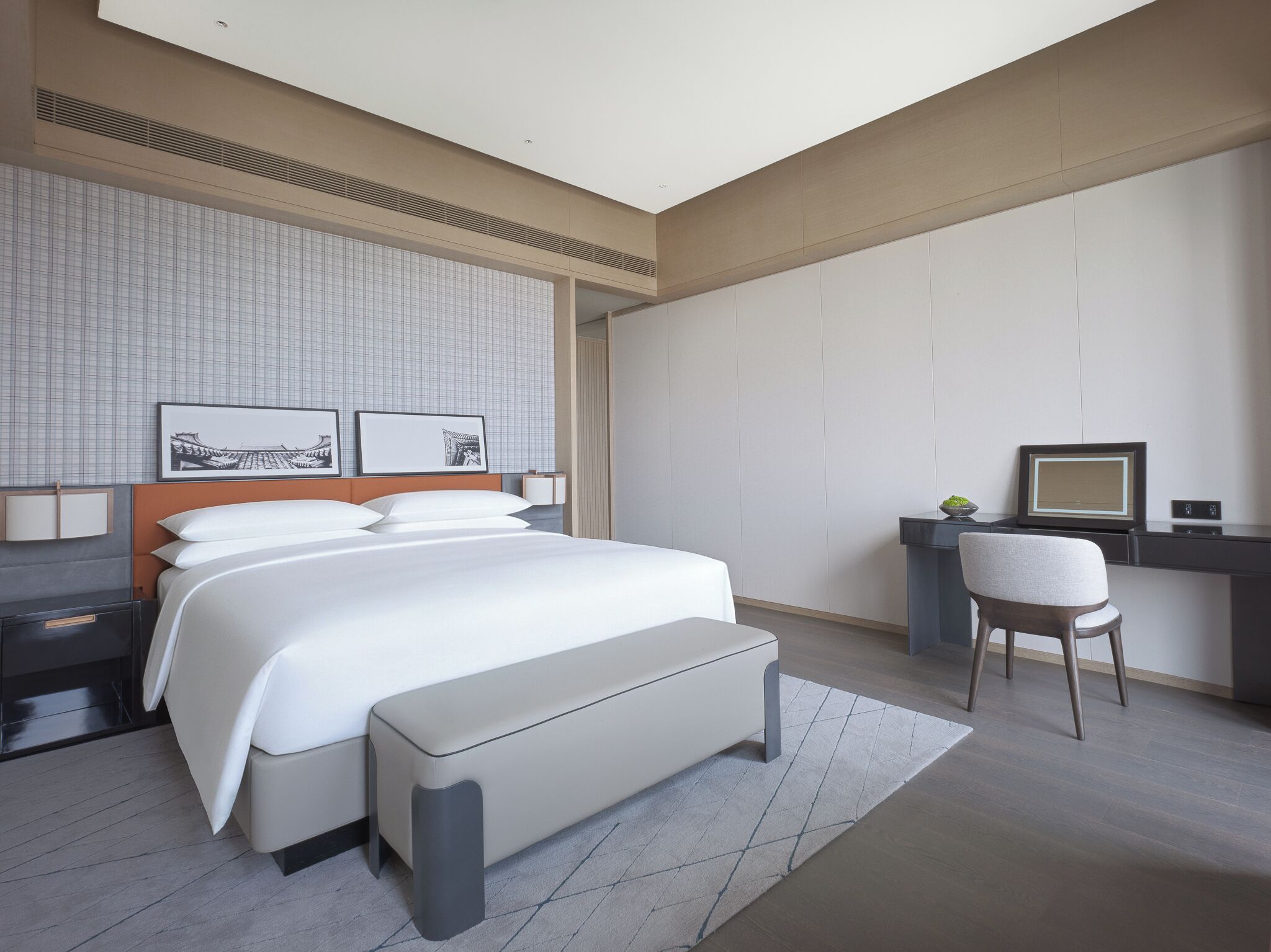 A modern hotel room with a large bed, a desk, a chair, and a television.