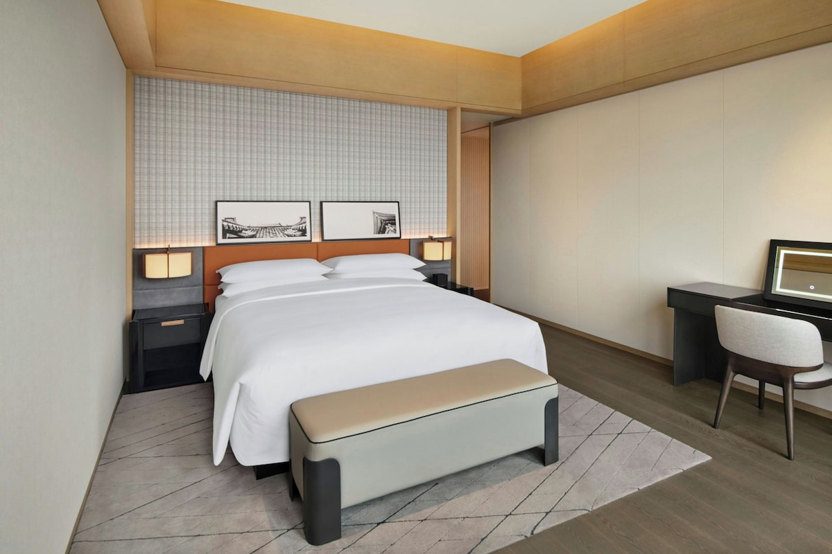A modern hotel room with a bed, bedside tables, a desk, and a chair.