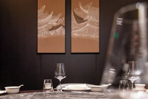 A dining table set with plates, bowls, and glasses, with two framed artworks on the wall behind.