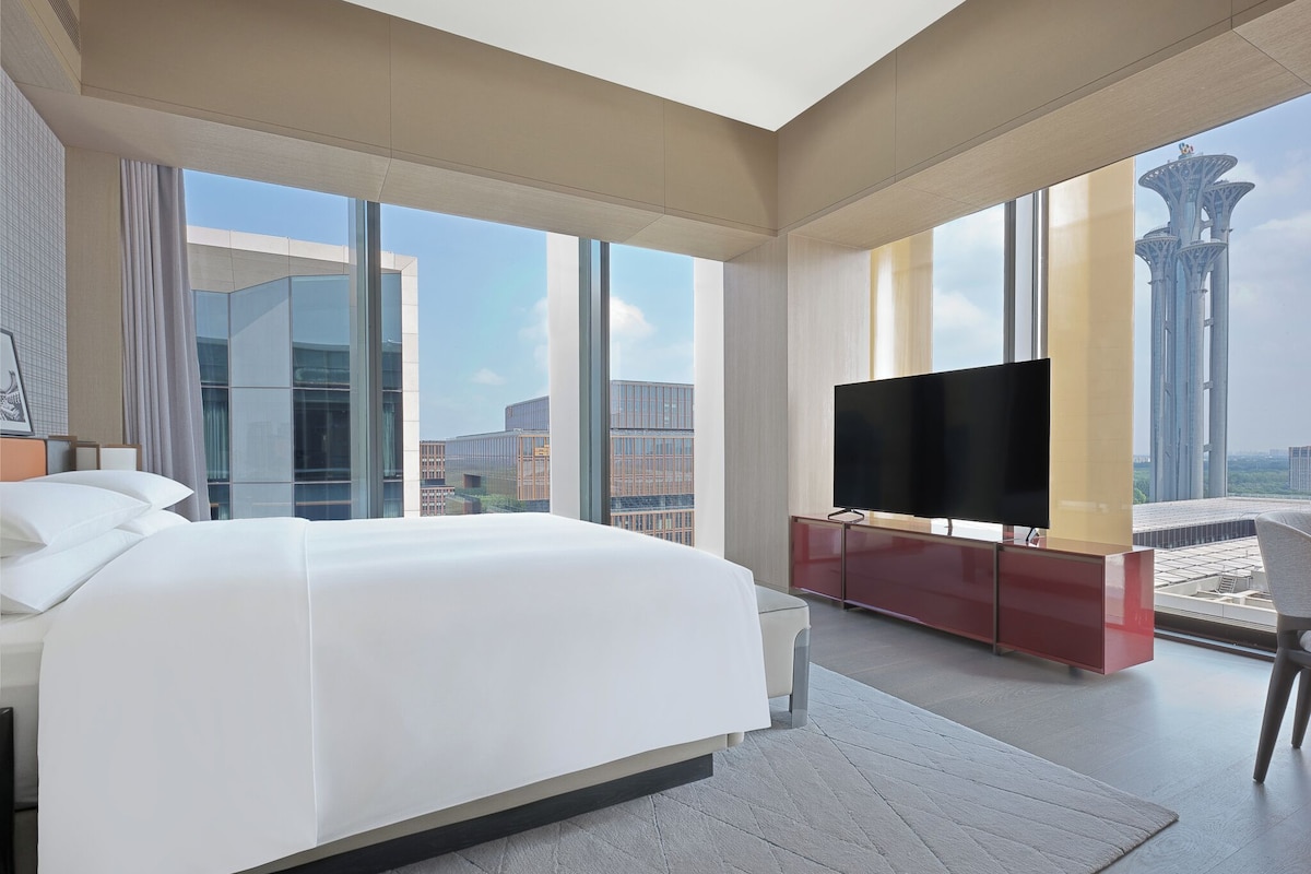 A modern hotel room with a large bed, a flat-screen TV, and a city view.