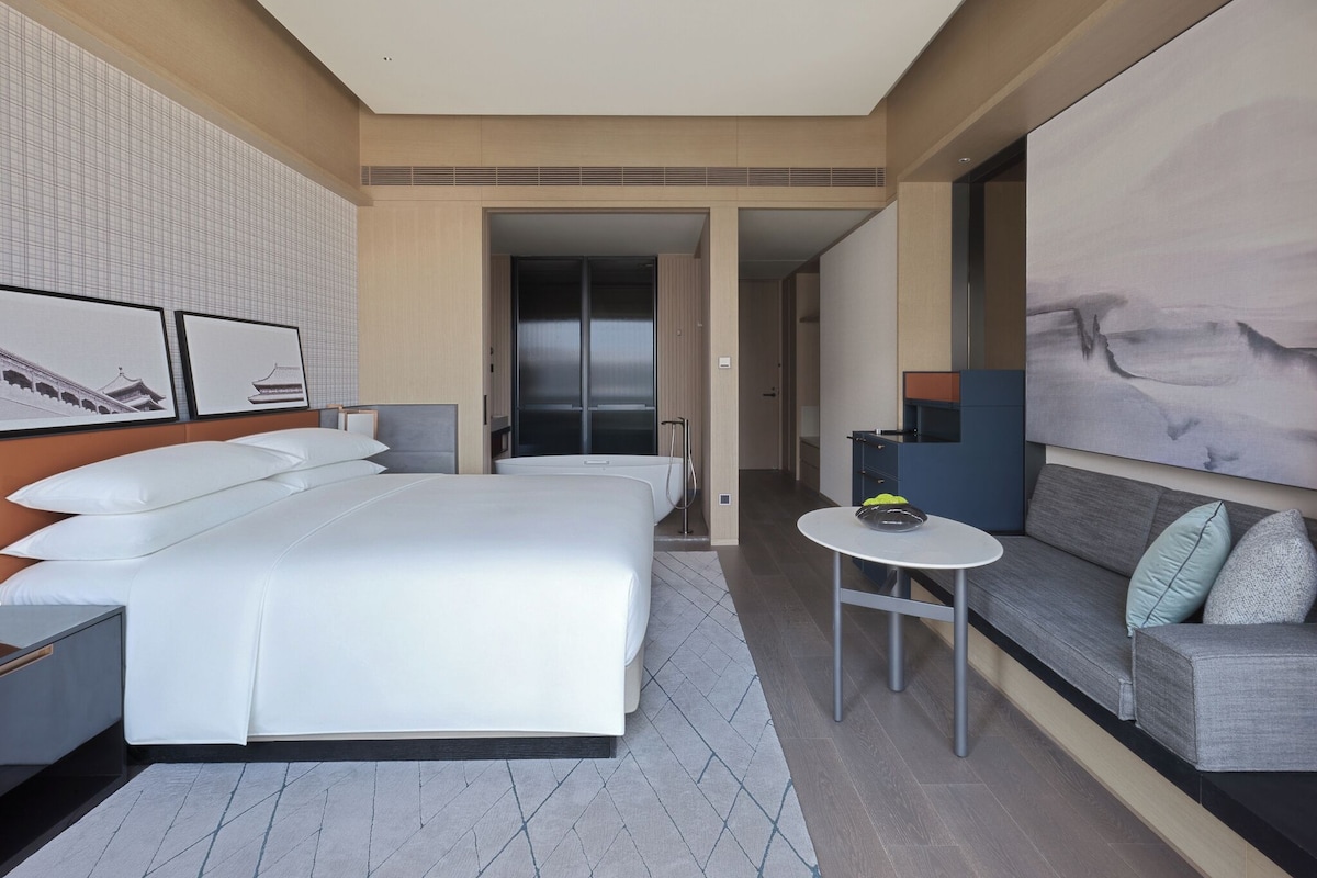 A modern hotel room with a large bed, a sofa, a small table, and artwork on the walls.