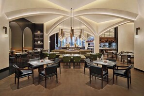 A modern restaurant with a central seating area, high ceilings, and a view of the city.