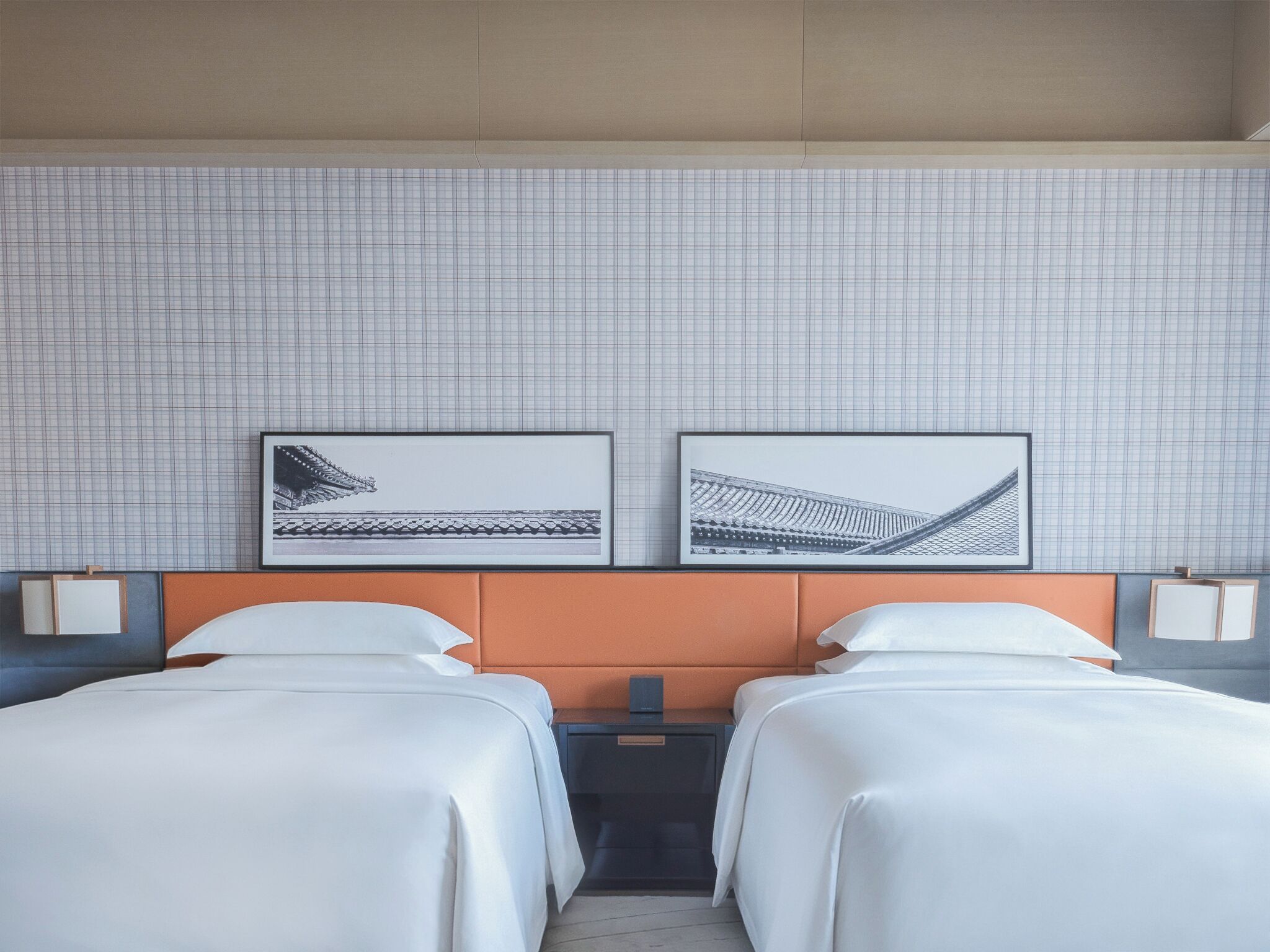 A hotel room with two beds, a tiled wall, and two framed pictures.