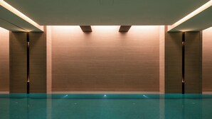 Una piscina con piso y paredes de azulejos, rodeada de muros con iluminación empotrada.