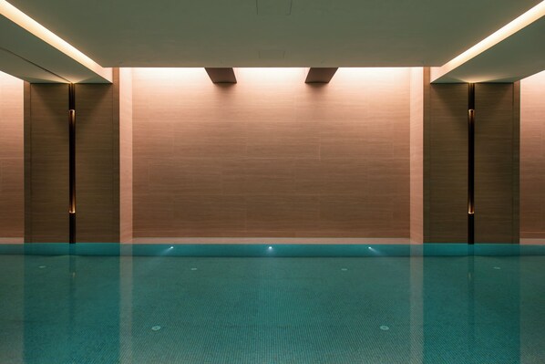 A swimming pool with a tiled floor and walls, surrounded by walls with recessed lighting.