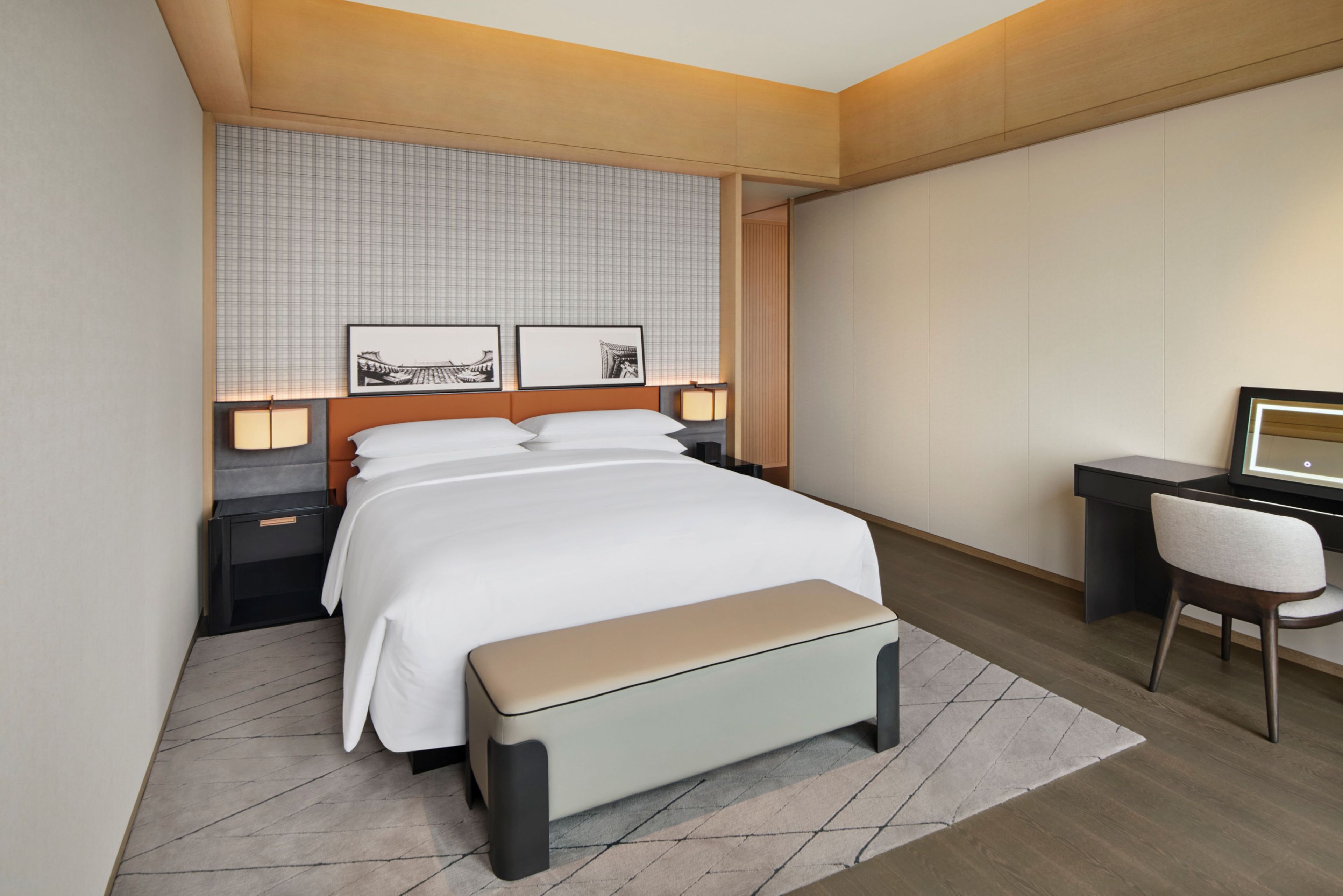 A modern hotel room with a bed, bedside tables, a desk, and a chair.
