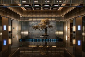 A modern lobby with a central water feature, reflective floor, and a large wall with a textured pattern.