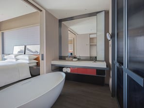 A modern hotel room with a large bed, a bathroom with a mirror, and a view of a building.