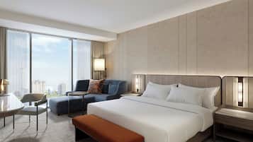 A hotel room with a large bed, a sitting area with a sofa and armchair, a small table, and a view of the city.
