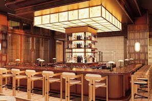 A bar area with a central island, multiple shelves of bottles, and bar stools.