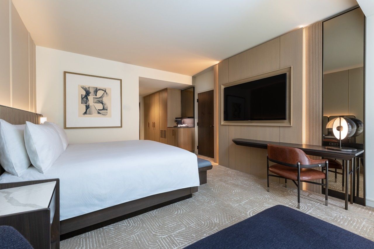 A hotel room with a large bed, a desk with a chair, a flat-screen TV, and a framed artwork on the wall.