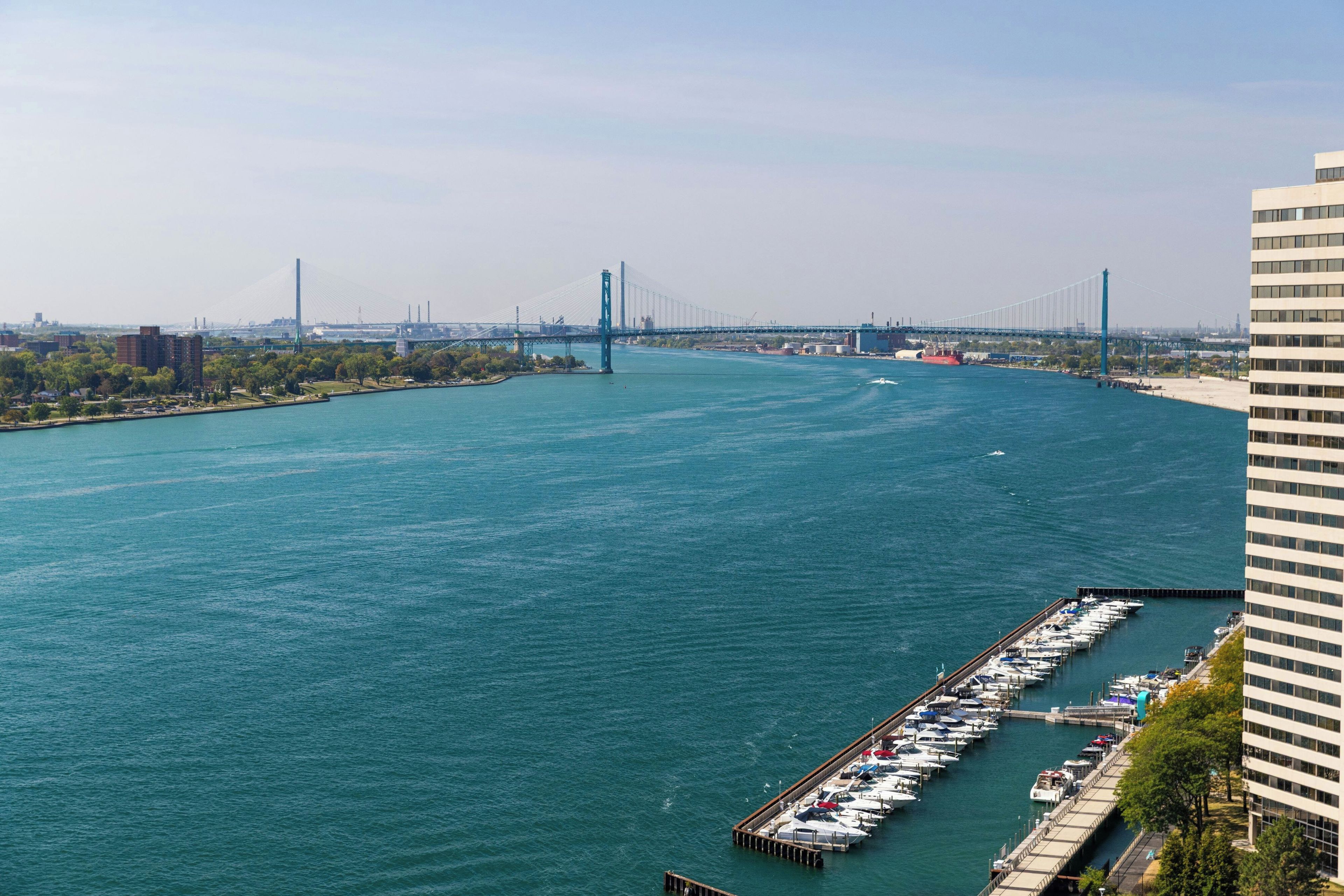 Una marina con barcos amarrados, un puente al fondo y un edificio a la derecha.
