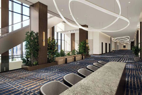 A spacious hotel lobby with a long reception desk, seating area, and large windows allowing natural light.
