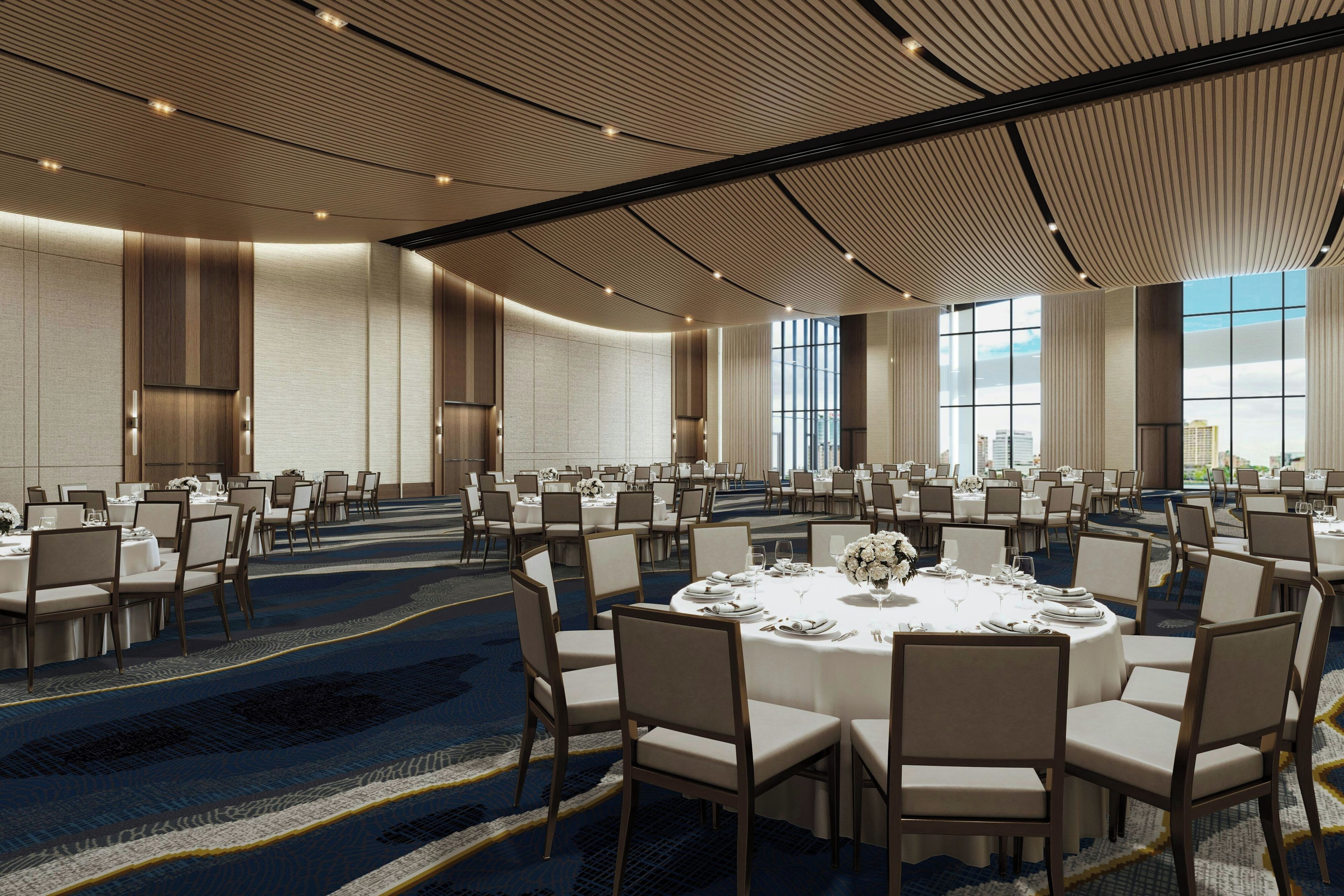A large conference room with round tables and chairs, high ceilings with a ribbed design, and large windows allowing natural light.
