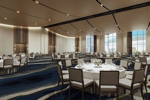A large conference room with round tables and chairs, high ceilings with a ribbed design, and large windows allowing natural light.