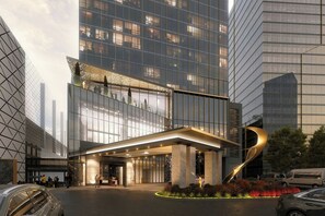 A modern hotel entrance with a glass facade, a prominent curved sculpture, and a landscaped garden area.