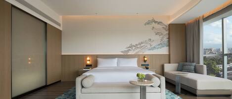 A modern hotel room with a large bed, a sofa, a small table, and a city view.